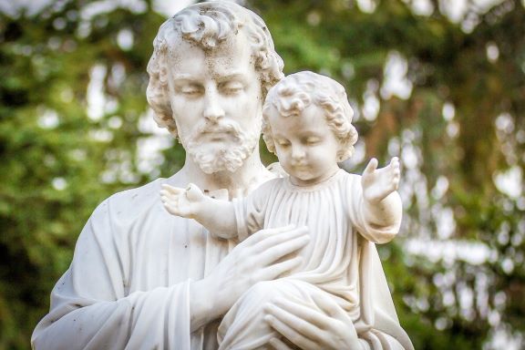 Statue of St. Joseph with baby Jesus with the backdrop of green trees